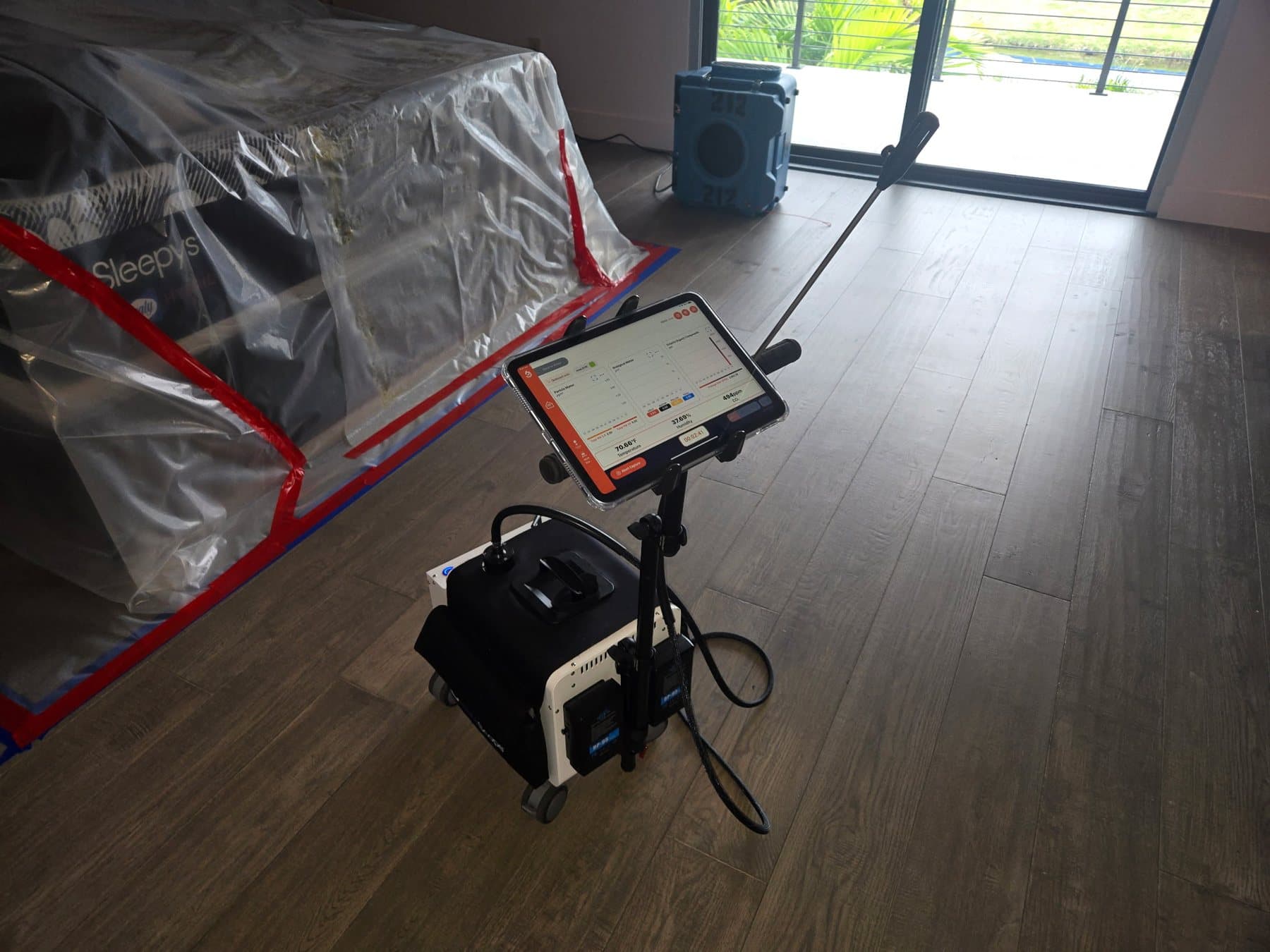 InstaScope air monitor running beside a plastic-wrapped, taped-off mattress and an air scrubber during a clearance visit
